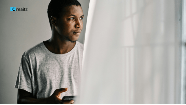 Young man holding smartphone and looking thoughtfully into the distance, representing ambition, career growth, personal development, digital skills learning, and future opportunities.